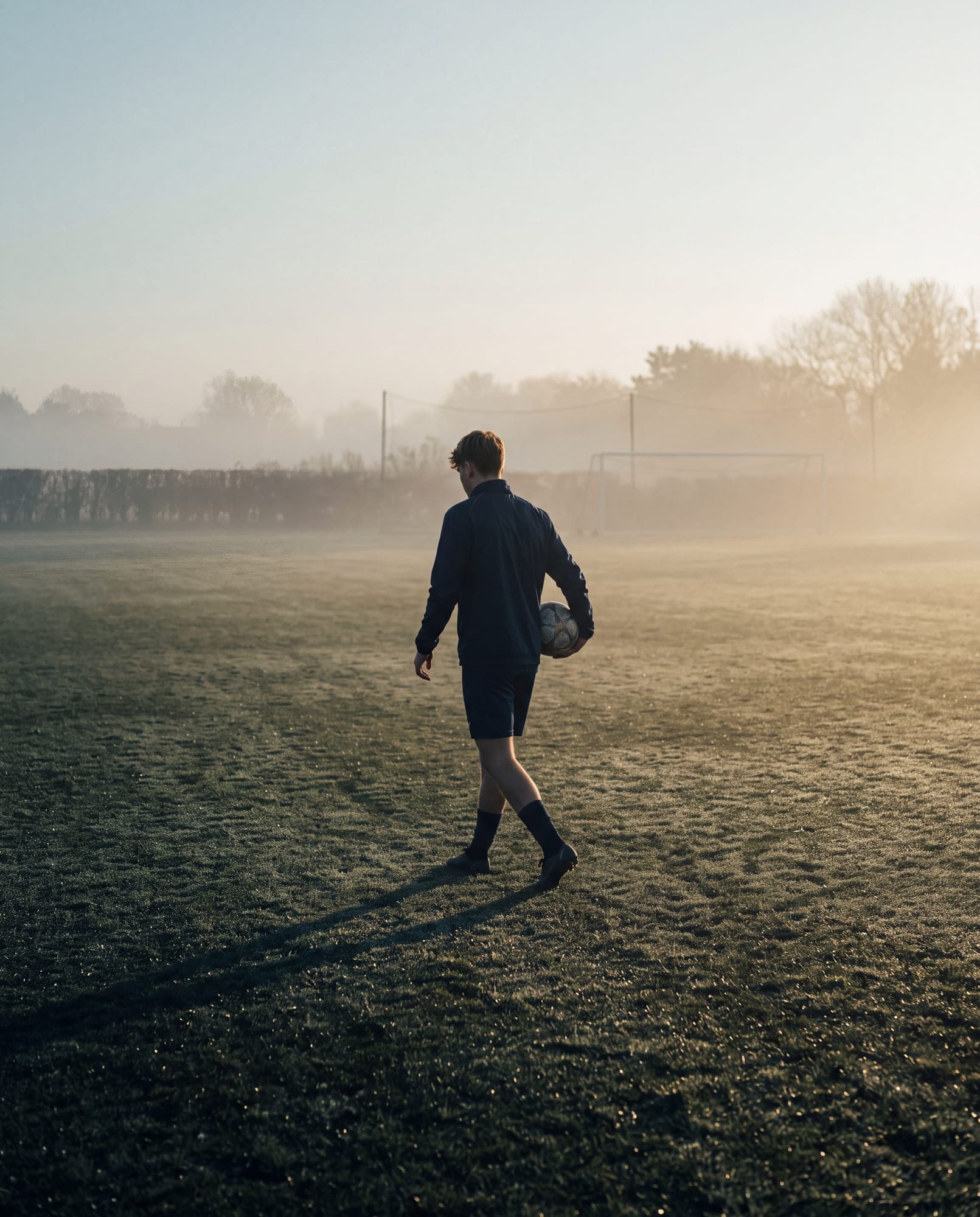 Junger Fußballer allein auf dem Trainingsplatz im frühen Morgenlicht